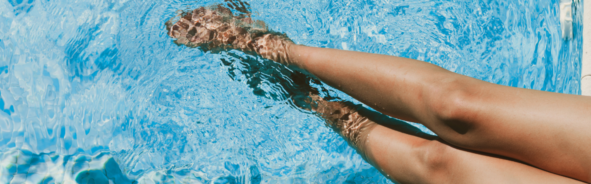 A lady's legs dangle in a pool.
