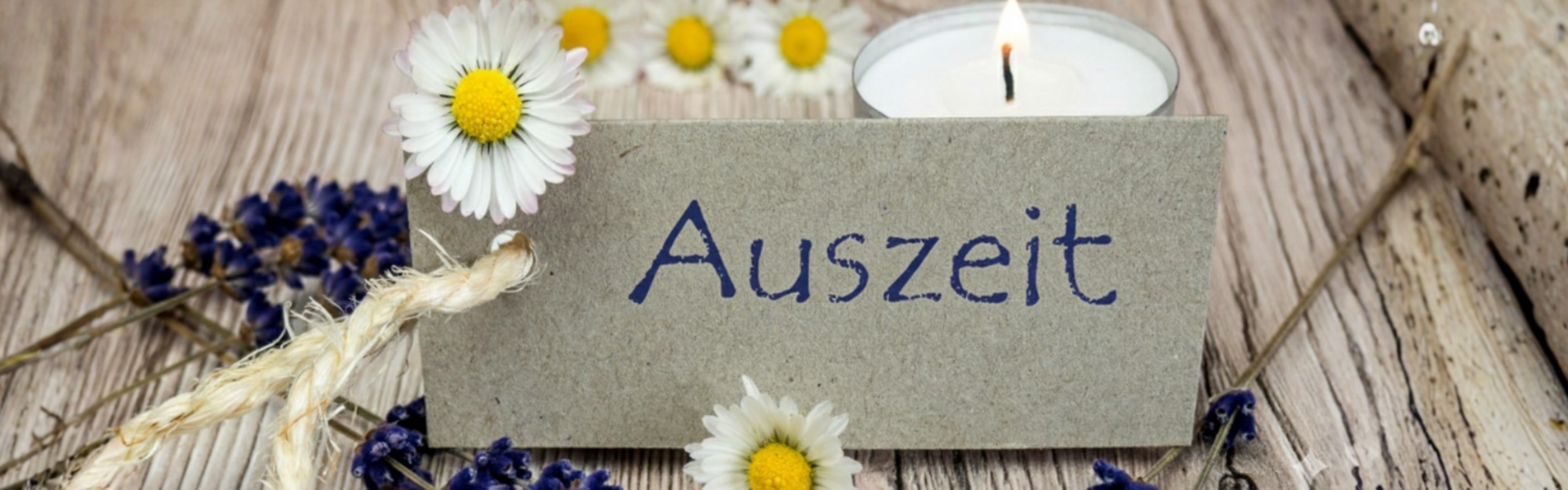 Sign with the words "Auszeit" and flowers and candle as decoration.